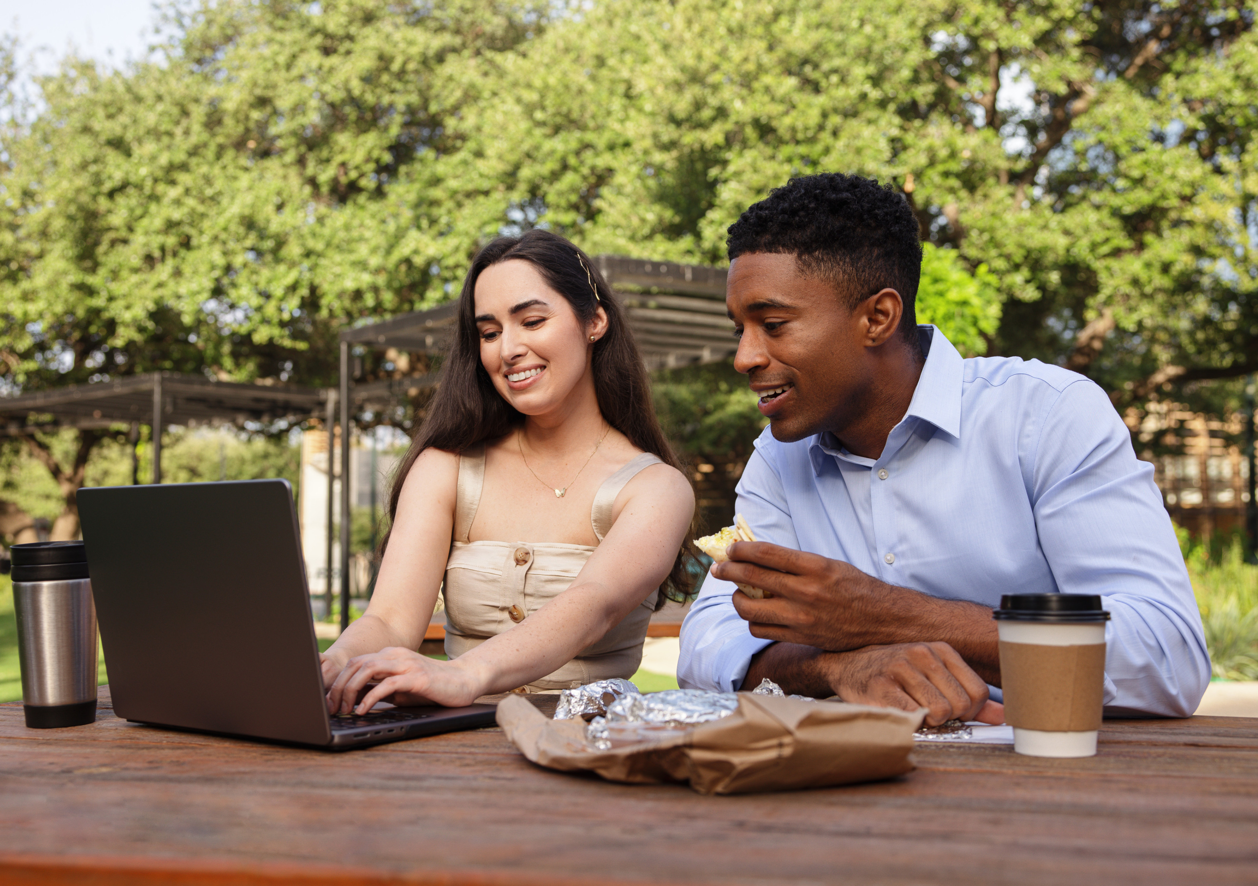 couple eating lunch and looking at computer in park